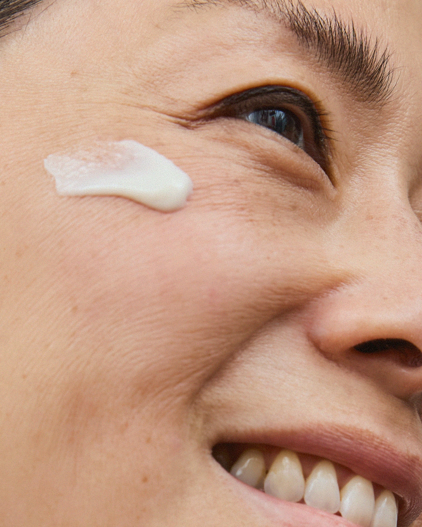 Close-up of a smiling woman's face with a dollop of white cream applied to her cheek.