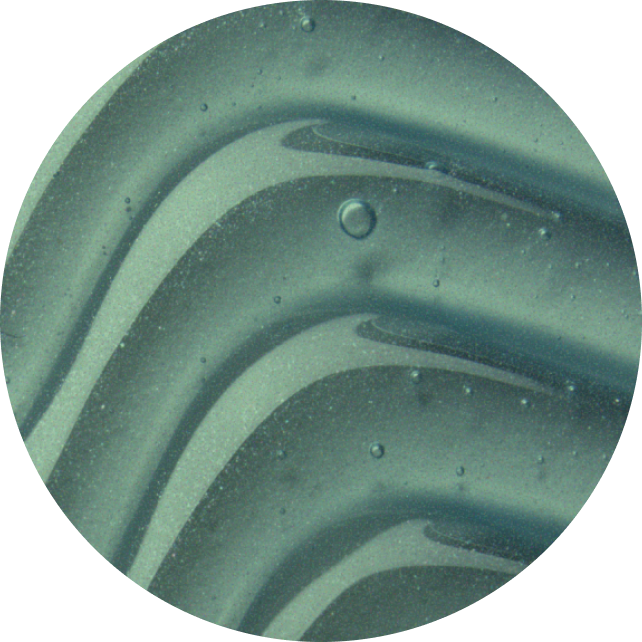 A close-up circular view of a glossy, curved surface with a muted teal-green sheen and small visible bubbles or imperfections.